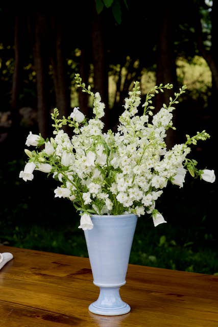 White flowers in a light blue vase on a wooden table with a blurred natural background