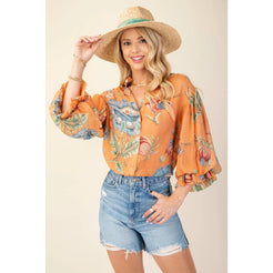 Woman wearing a floral blouse and denim shorts with a straw hat on a beige background
