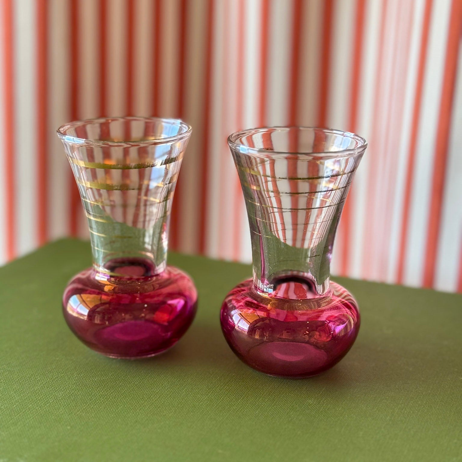 Two pink-bottomed glass tumblers on a green surface with a striped background