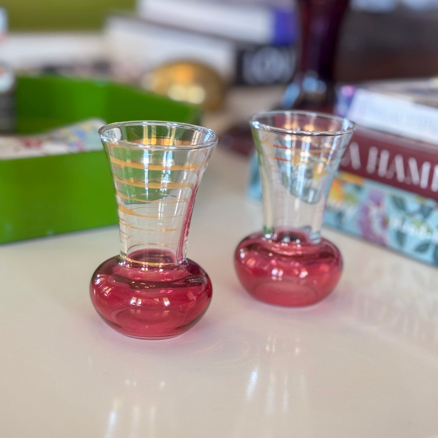 Two small glass shot glasses with red bases on a light surface.