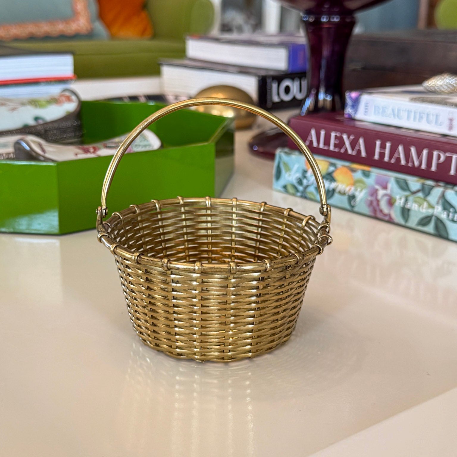 Small gold wicker basket on a surface with books and a green box in the background