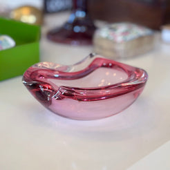 Pink glass ashtray on a white surface with blurred background