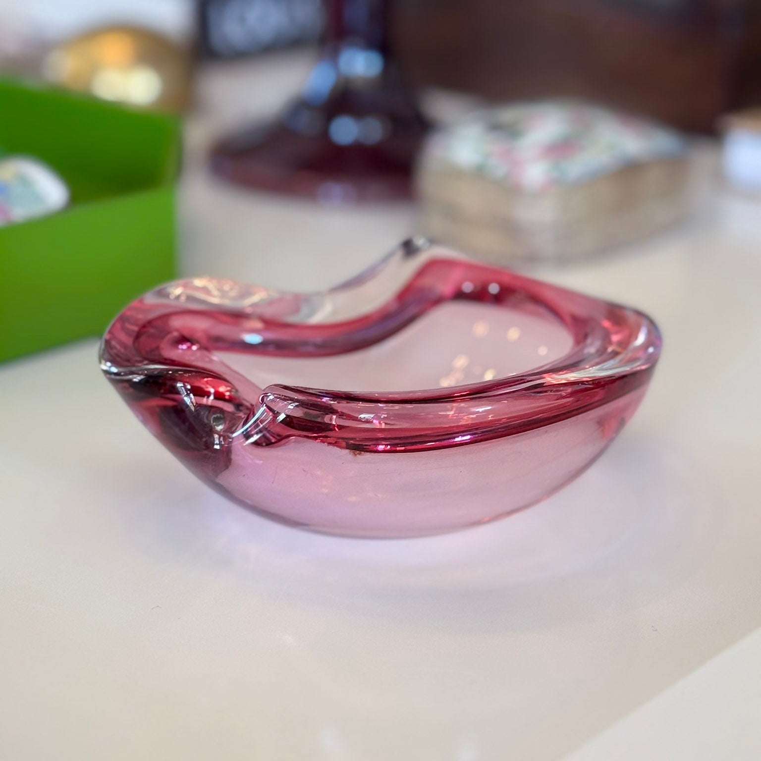 Pink glass ashtray on a white surface with blurred background